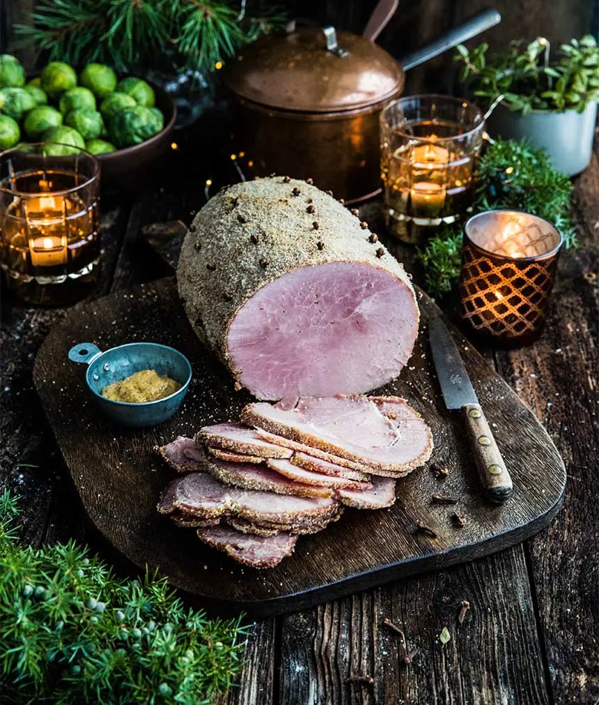 Griljerad julskinka med kryddnejlika, skivad på en mörk träskärbräda