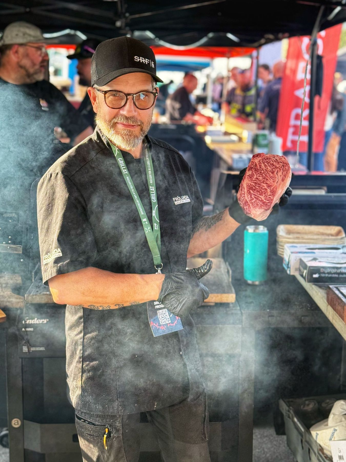Ove Feeser i röken vid grillen, med en bit wagyu i handen