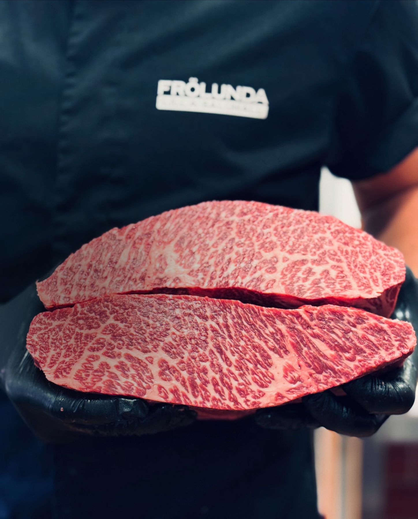 Styckmästare i Frölunda Lilla Saluhalls uniform håller två skivor högmarmorerad wagyu